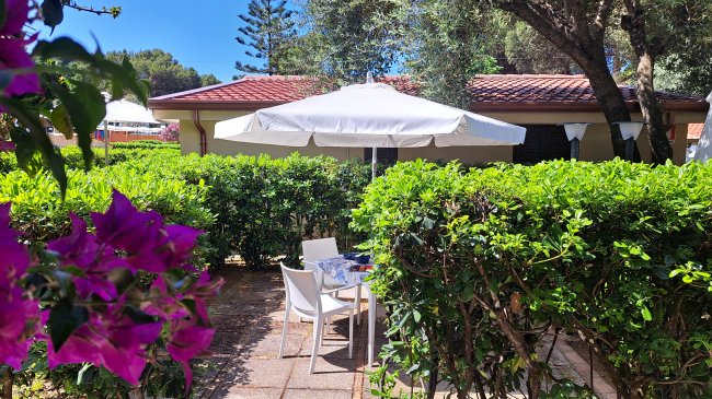 Tavolo e sedie in giardino, con ombrellone bianco e fiori viola.