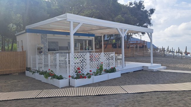 Struttura bianca su spiaggia con tettoia e fioriere.