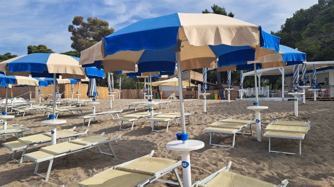 Ombrelloni blu e beige su spiaggia con lettini.
