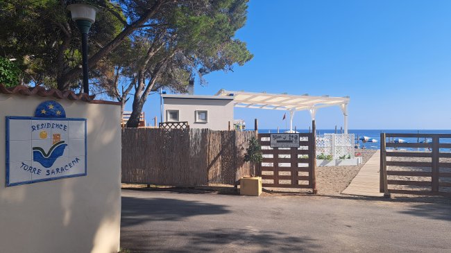 Ingresso di una residenza vicino al mare, con cartello e cancelli in legno.