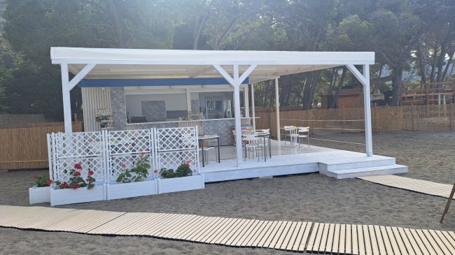 Struttura bianca su una spiaggia con sedie e tavoli sotto una tettoia.