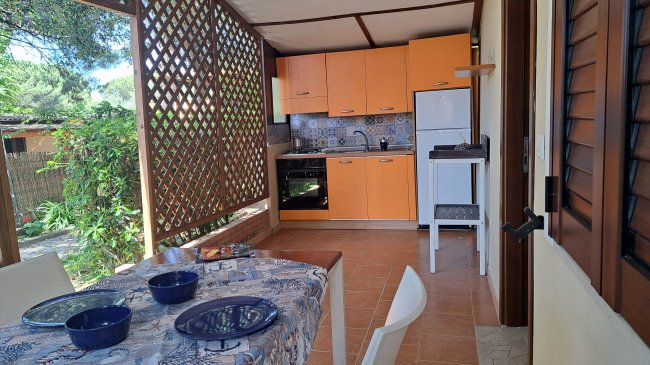 Cucina all'aperto con pareti a grata, tavolo apparecchiato, e mobili arancioni.
