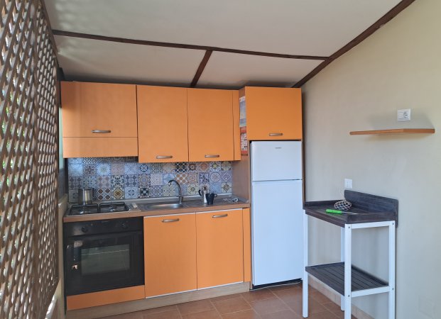 Cucina con mobili arancioni, piastrelle decorate e un frigorifero bianco.