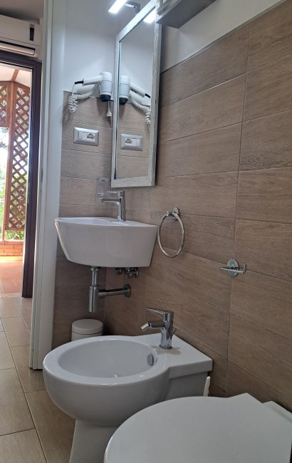 Bagno moderno con lavabo, bidet, specchio e asciugacapelli a muro.