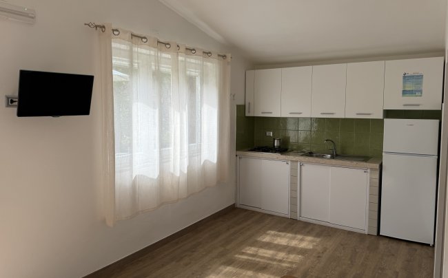 Cucina minimalista con mobili bianchi, piastrelle verdi e tende trasparenti.