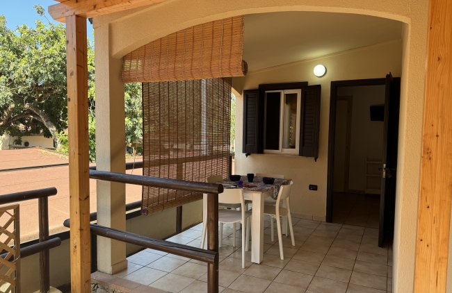 Terrazza arredata con tavolo e sedie bianche, divisorio in bambù e pavimento piastrellato.