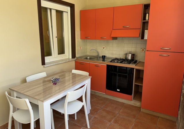 Cucina con mobili arancioni, tavolo in legno chiaro con quattro sedie bianche.