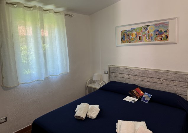 Camera con letto a due piazze, quadro colorato e tende bianche luminose.