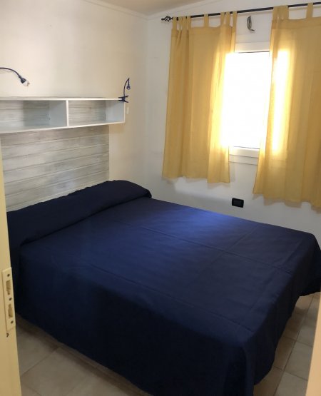 Camera con letto matrimoniale coperto da una trapunta blu, finestre con tende gialle.