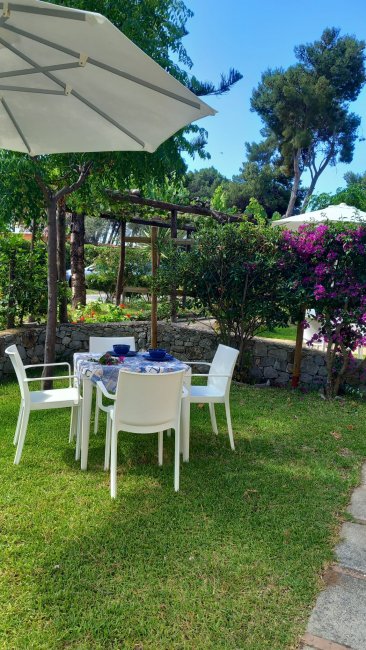 Tavolo da giardino con sedie bianche e ombrellone.