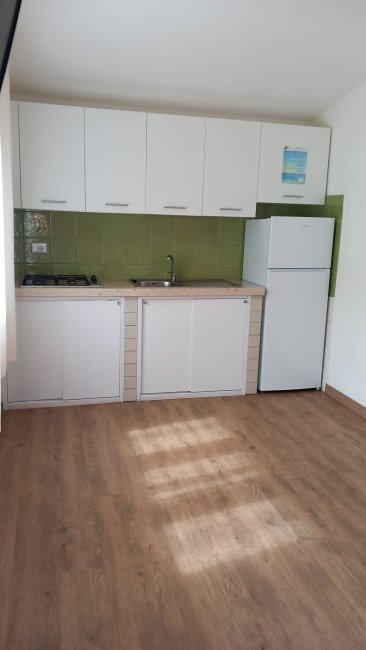 Cucina compatta con frigorifero e mobili bianchi.