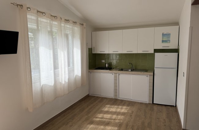 Cucina luminosa con mobili bianchi e tenda chiara.