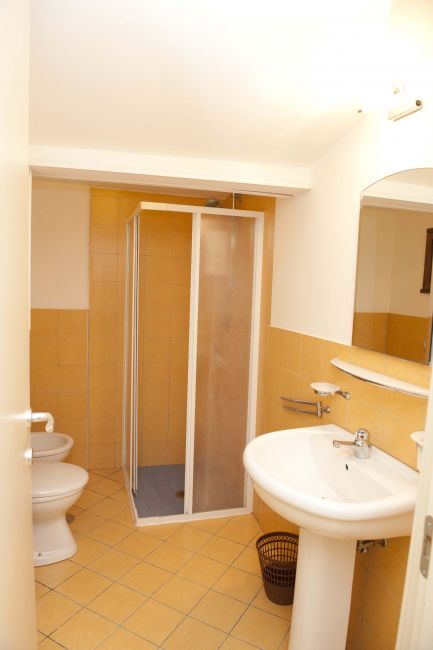 Bagno con doccia, lavabo bianco, bidet e piastrelle gialle.