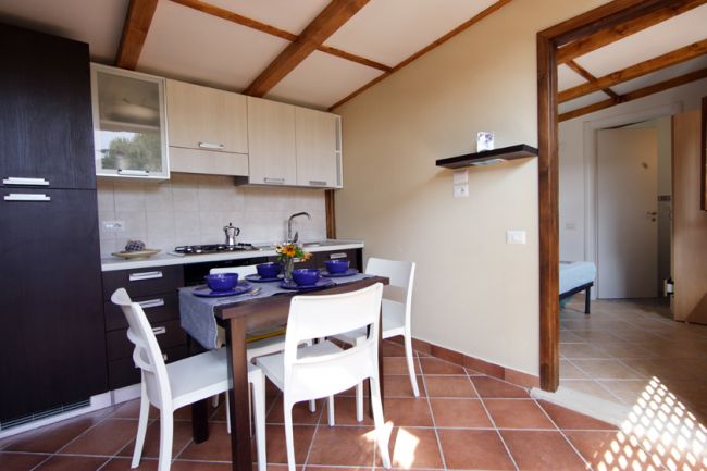 Cucina moderna con tavolo apparecchiato, sedie bianche e mobili in legno scuro.