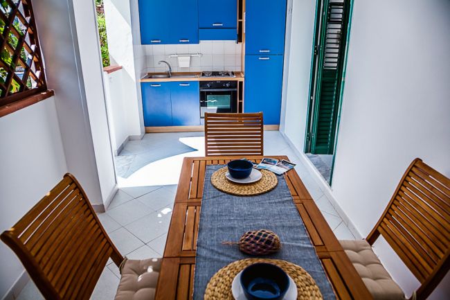 Tavolo da pranzo in legno con stoviglie, cucina blu sullo sfondo.