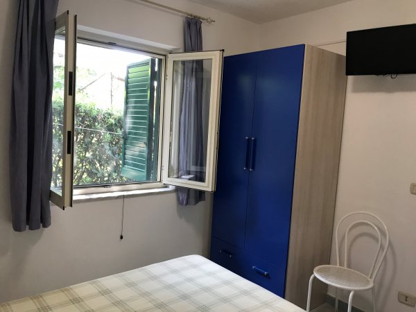 Camera con letto, finestra aperta, armadio blu e sedia bianca.