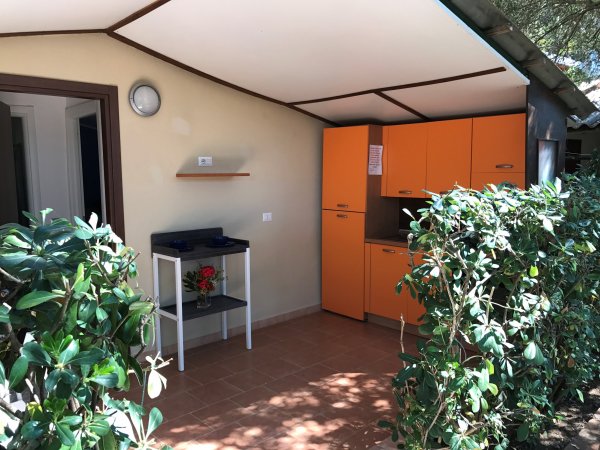 Cucina esterna con mobili arancioni, piante e pavimento in cotto.