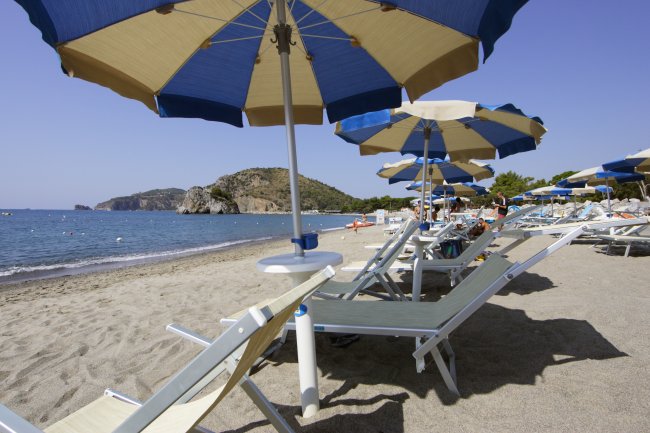 Spiaggia con ombrelloni blu e gialli, lettini e mare calmo.