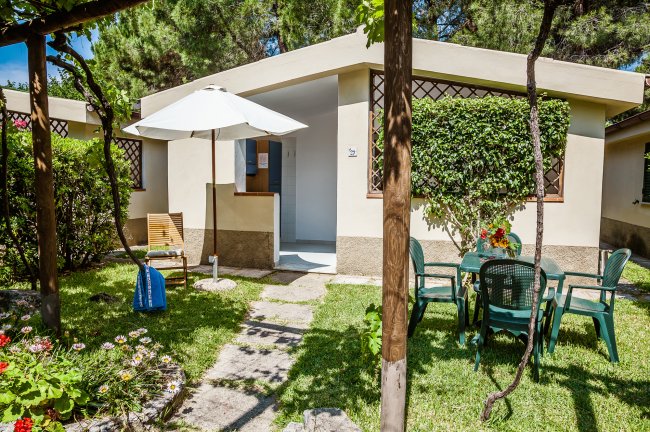 Patio con tavolo, sedie e ombrellone bianco nel giardino di una casa.