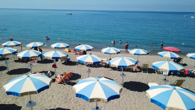Ombrelloni bianchi e blu su una spiaggia di sabbia davanti al mare.