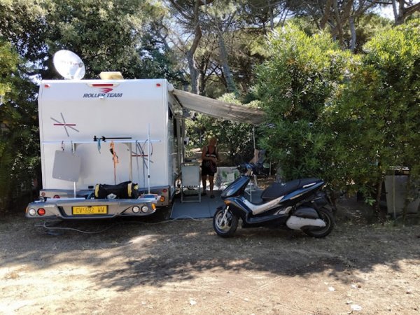 Camper e motorino accampati tra alberi.