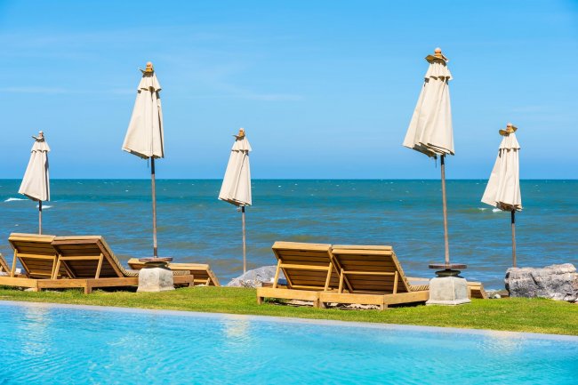 Lettini e ombrelloni sul mare con piscina in primo piano.