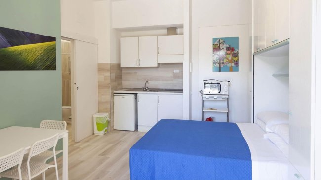 Monolocale con letto, angolo cottura e tavolo, arredamento semplice.