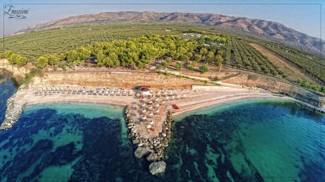 Una spiaggia con ombrelloni e mare cristallino, vista dall'alto.