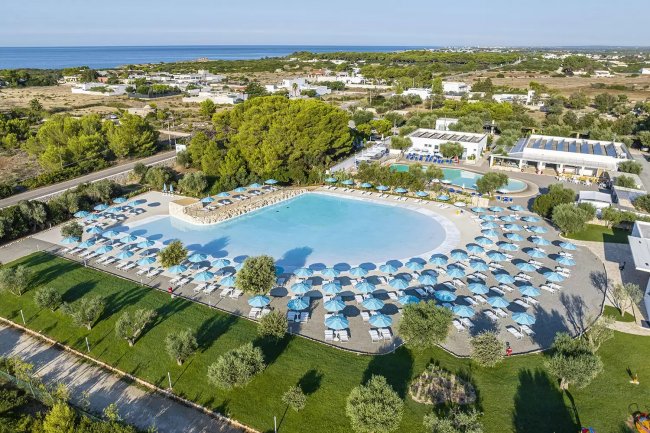 Grande piscina con ombrelloni e paesaggio verde.
