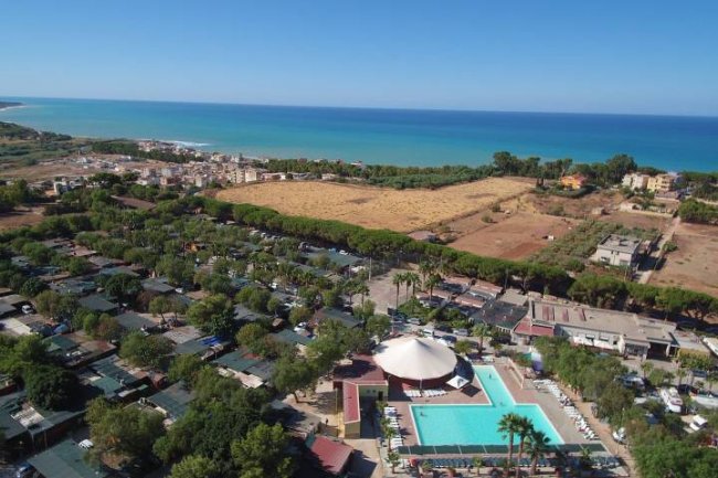 Vista aerea di un villaggio turistico con piscina vicino al mare.