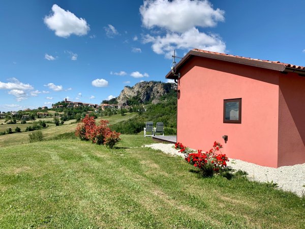 Casetta rosa su prato con cespugli e cielo blu.