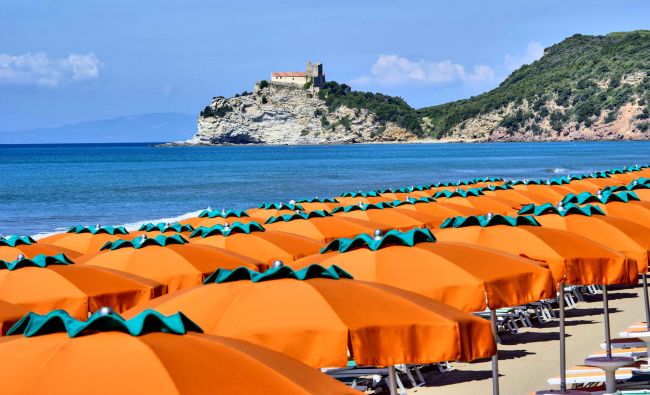 Spiaggia con ombrelloni arancioni e vista su castello su una scogliera.