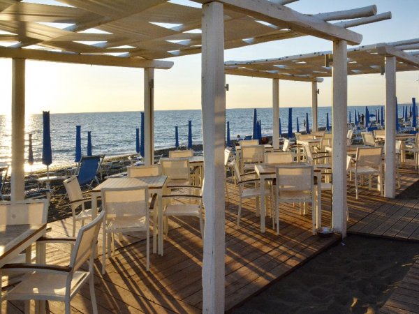 Ristorante all'aperto in riva al mare con sedie bianche.