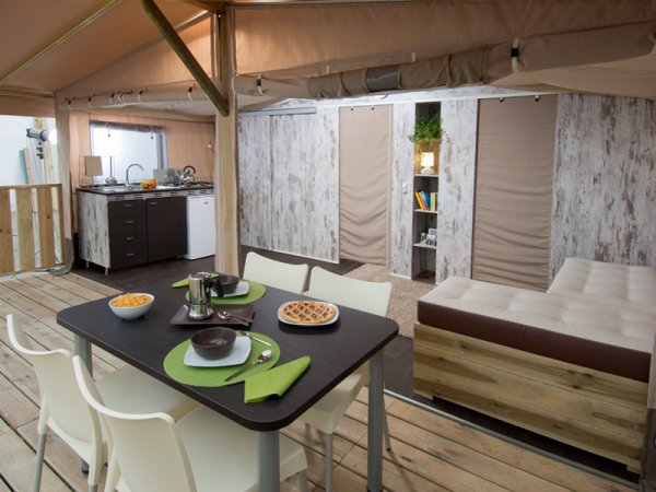 Interno di una tenda con tavolo apparecchiato e cucina.