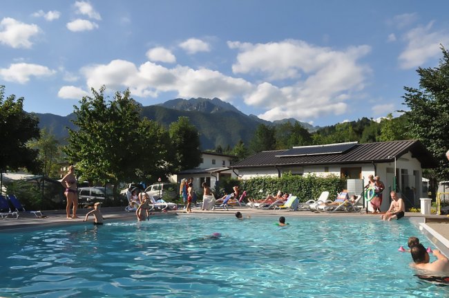 Piscina all'aperto con persone, montagne sullo sfondo.