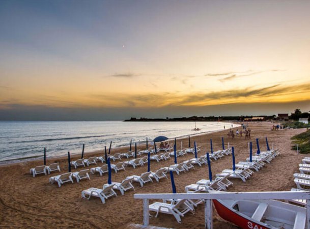 Spiaggia al tramonto con lettini e passerella.