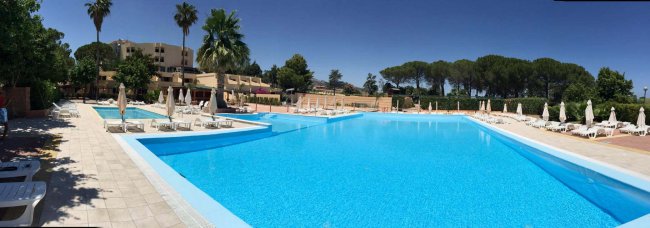 Piscina grande con lettini e ombrelloni bianchi.