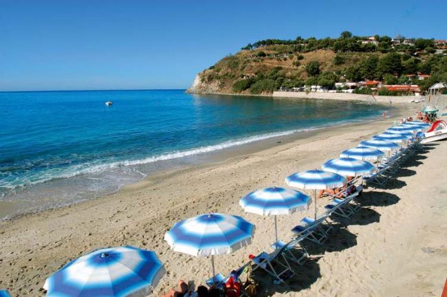 Spiaggia con ombrelloni bianchi e blu vicino al mare limpido.