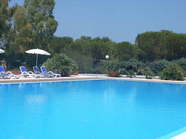 Ampia piscina all'aperto con lettini e ombrelloni, circondata da alberi.