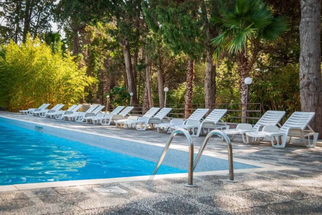 Piscina con lettini bianchi e sfondo di alberi.