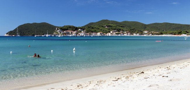 Spiaggia sabbiosa con mare e colline sullo sfondo.
