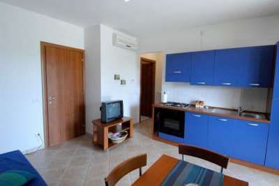 Una cucina blu con tavolo e sedie, TV su mobile e porta di legno.