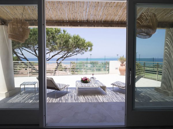 Terrazza vista mare con lettini e tavolino, circondata da alberi.