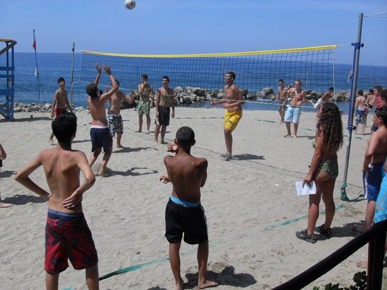 Persone giocano a pallavolo su una spiaggia di sabbia vicino al mare.