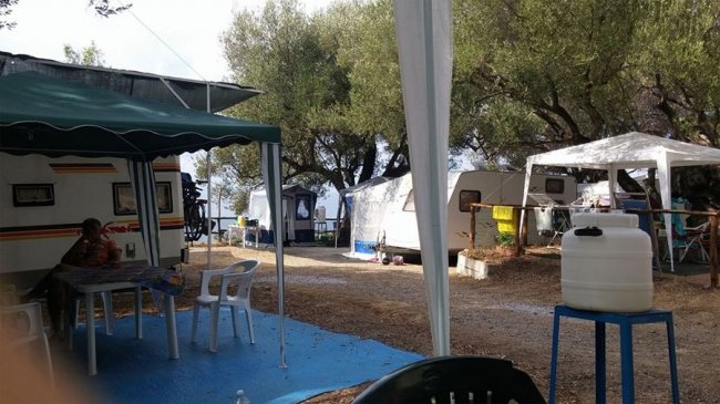 Area campeggio con roulotte e gazebo sotto alberi, tavoli e sedie da esterno.