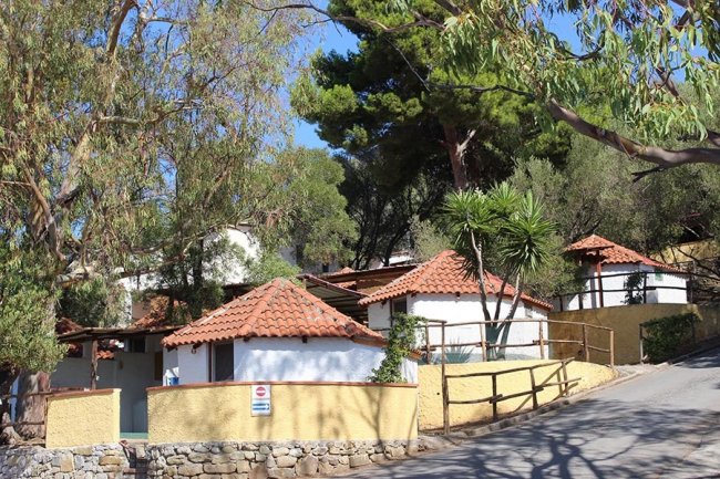 Casette bianche con tetti in tegole rosse, immerse tra alberi e piante.