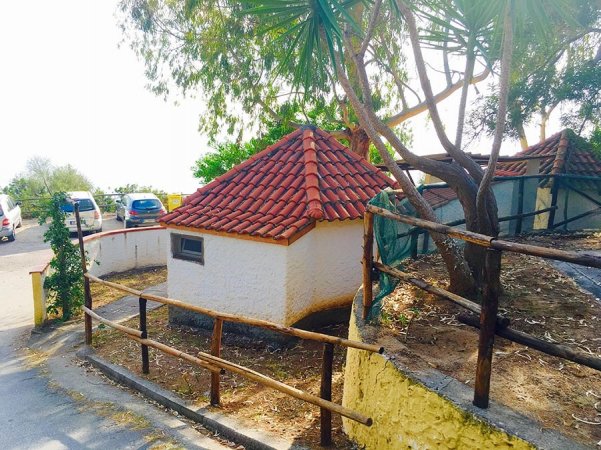 Piccola costruzione con tetto rosso circondata da alberi e staccionata.