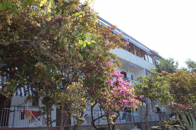 Edificio bianco con fiori colorati in primo piano e tende a righe.