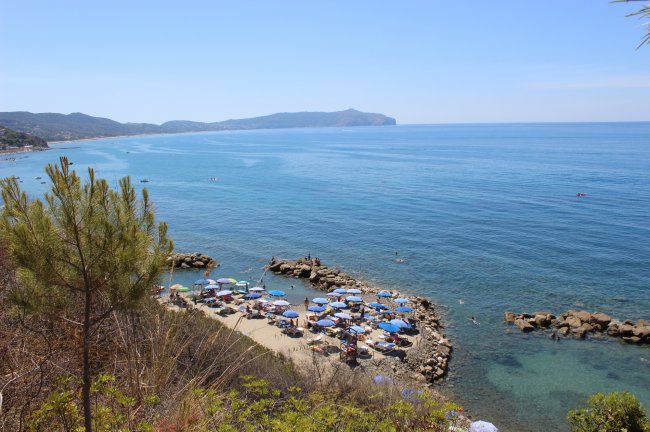 Spiaggia con ombrelloni e vista panoramica sul mare e promontori lontani.