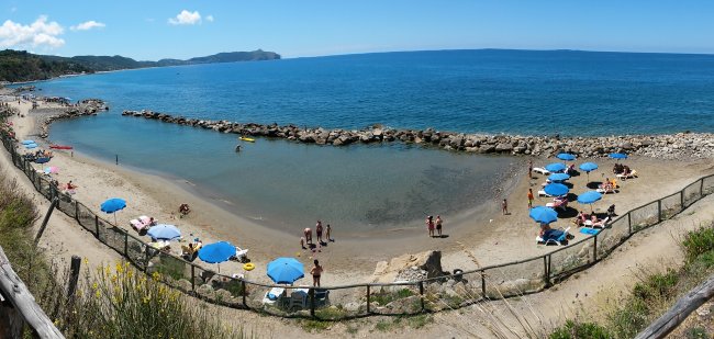 Spiaggia con ombrelloni blu e scogliere, acqua tranquilla delimitata da rocce.